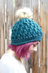 person wearing a teal alpine stitch crochet beanie with a faux fur pom pom outdoors thumbnail