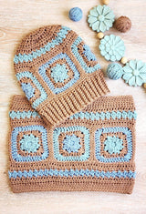 Tan blue crochet hat and cowl on wooden surface with blue carved flowers. thumbnail