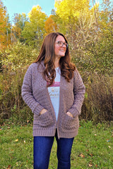 Brunette woman wears tan crochet cardigan in front of fall trees. thumbnail