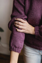 Close up of the sleeve of a knit purple sweater, worn with light color jeans. thumbnail