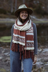 Woman wears cream, red, rust shawl wrapped around neck, standing in front of water. thumbnail