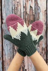 Close up of mittens in pink, cream, and green, modeled in front of weathered barn door. thumbnail