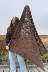 Woman holding brown mesh lattice afghan diagonally in front of body, on boardwalk. thumbnail