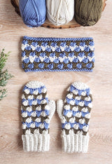 Crochet mittens in cream, blue, and brownish olive and matching headband laid on pale wood table. thumbnail