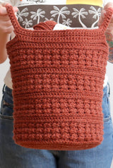 Woman holds tall crochet basket toward camera, holding it by two side handles. thumbnail