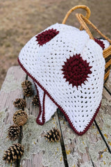 Crochet blanket folded in wicker basket, sitting on wooden picnic table with a collection of pinecones. thumbnail