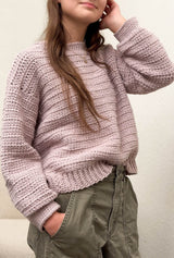 Side front view of pale pink crochet sweater, slightly oversized, worn with khaki pants. thumbnail