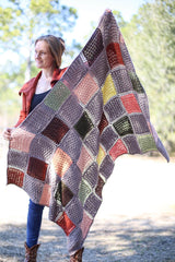 Full view of crochet lapghan, held out toward camera by woman in rust jacket, blue jeans, and boots. thumbnail