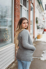 Back side view of woman wearing crochet cardigan on snowy small town sidewalk. The drop shoulder construction and shoulder seam is visible. thumbnail