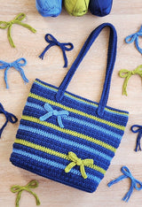 Top down view of bag on pale background. It's surrounded by bows made of yarn strands, in navy, pale blue, and green-yellow to match bag colors. thumbnail
