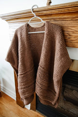 Ruana style poncho on a hanger, hanging from a wooden mantelpiece. thumbnail