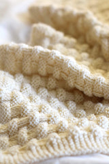 Close up of rumpled cream knit blanket laying on a white background. thumbnail
