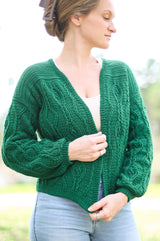 Woman looks to the side while wearing an emerald green crochet cardigan, open at the front with no buttons. thumbnail