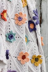 Close up of 3D crochet flowers of various types, in multi-colors, on a white crochet blanket. thumbnail