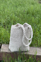 Crochet tote bag sits upright on a railroad tie. It's heavily textured and has two handles. thumbnail
