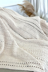 Cream crochet blanket laid open over couch, showing bands of different textures. thumbnail