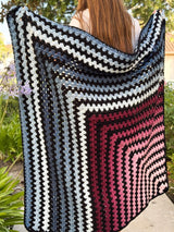 Mitered square crochet blanket held by woman standing outside on patio. thumbnail