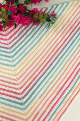 Flat lay photo of shawl on a white table top, with a bouquet of pink flowers at the top edge. thumbnail