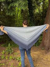 Back view of woman holding large triangular shawl with top edge outstretched. thumbnail