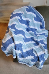 Crochet afghan with wave motif in blues and white laid on plush couch indoors. thumbnail