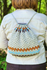 Crochet string backpack worn by woman in cream jacket. The bag is smaller than her back, cinched at the top. thumbnail