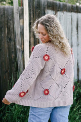 Back view of crochet cardigan worn over jeans. The cardigan body is a warm grey, with rust and pink flowers at the center of some squares. thumbnail