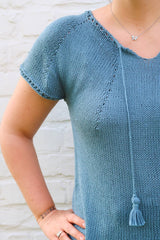 Close up of front of knit top, showing increase lines, split collar, and tassel trim. thumbnail