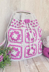 Crochet bag standing up on wooden plank table, filled and with top cinched. thumbnail