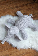 Top down view of crochet stuffed elephant sitting on a fluffy white rug on a wooden floor. thumbnail