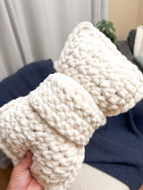Close up of crochet bow pillow held above armchair. thumbnail