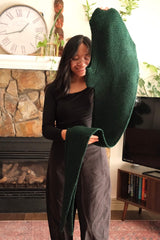 Woman holds hooded crochet scarf toward camera. thumbnail