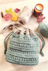 Flat lay of shoulder bag with drawstring cinched. There are two balls of yarn, an unlit candle, and fall leaves scattered around. thumbnail