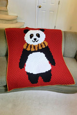 Red-orange afghan with a large panda draped over a light brown couch. thumbnail