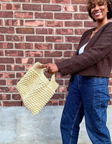 Woman holding butter yellow crochet bag with bobble stitches in front of brick wall thumbnail