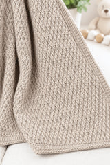 Neutral baby blanket draped on white couch thumbnail