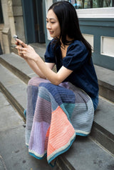 woman on her phone with a crochet blanket draped on her lap thumbnail