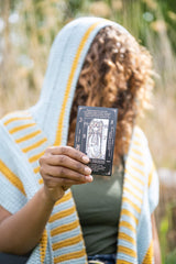 Woman wearing yellow and blue hooded scarf holding tarot card thumbnail