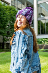 Woman wearing purple and multicolor striped hat with pom thumbnail