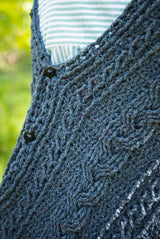 closeup view of dark grey textured cable-knit pattern and dark buttons on the buttoned wrap shawl worn over a striped shirt thumbnail