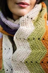 close-up of a person wearing a multicolored ripple-pattern scarf in purple, orange, green, and cream thumbnail