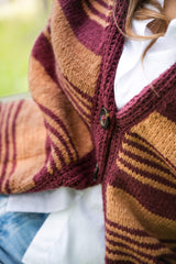 close-up of a striped brown and plum knit cardigan buttoned with a tortoiseshell button, layered over a white shirt thumbnail
