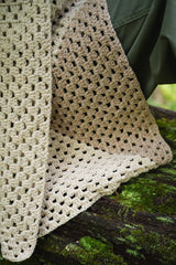 close-up of a cream granny square crocheted wrap draped over a mossy log outdoors thumbnail