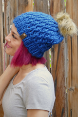 woman wearing a teal alpine stitch crochet beanie with a faux fur pom pom outdoors thumbnail