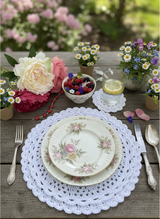 white crocheted circular scalloped edge placemat with a floral plate and silverware on a wooden table thumbnail