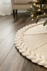 cream knitted Christmas tree skirt with a braided cable border flat laid on dark wood thumbnail