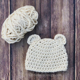 cream crocheted chunky bear beanie with ears and yarn on a wood background thumbnail