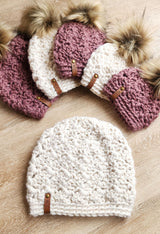 handmade white and dusty rose textured crochet beanies with faux fur pom-poms on a wooden surface thumbnail