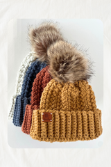 flat lay of 4 crochet hats with fur pom poms - gray, blue, rust, mustard thumbnail