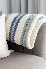 close-up of striped crocheted blanket draped over the arm of a grey sofa next to a white pillow thumbnail