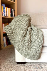 olive green knitted seersucker throw blanket draped over the arm of a beige armchair thumbnail